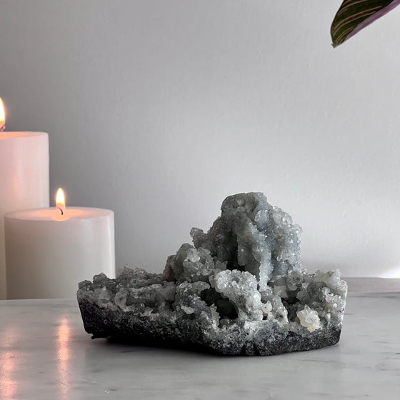 Decorative crystal piece on a marble surface with two lit candles and a plant leaf.