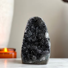  A polished black amethyst crystal with a cut base, placed on a flat surface with a candle in the background.
