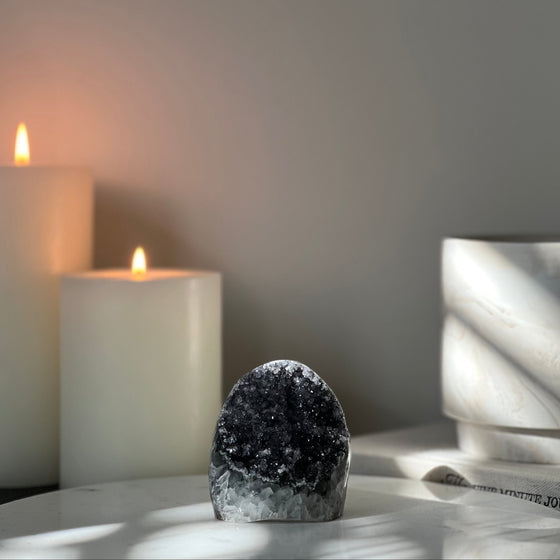 Black Amethyst Cut Base self standing on marble display with candles and a book in the background.
