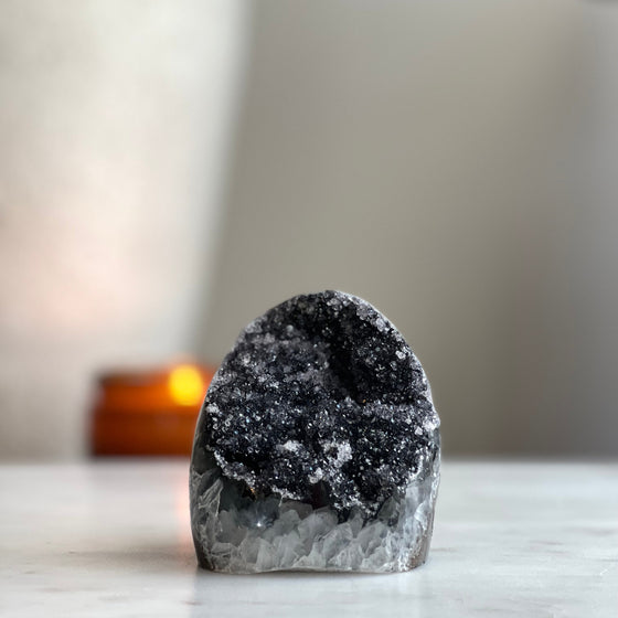 Black Amethyst Cut Base on marble platform with candle in the background.