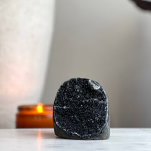  A polished black amethyst cut base stone, placed on a white surface with a candle in the background.