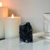 Black amethyst crystal on a marble surface with candles in the background