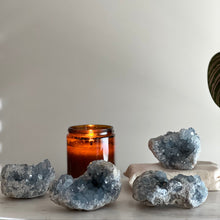  Crystal geode shapes with a lit amber candle on a neutral background.