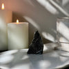 Decorative dark gray amethyst crystal on a white surface with candles and a glass container in the background.