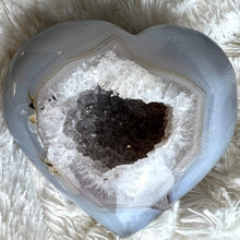  A heart-shaped agate stone with a druzy center, placed on a white furry surface.