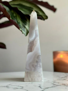  Druzy Agate Tower placed on marble stand with plant and candle in the background.