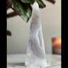Druzy Agate Tower placed on marble stand with plant and candle in the background.