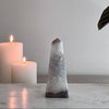 Decorative crystal obelisk and two white candles on a marble surface with a neutral background