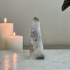 Decorative crystal obelisk with two candles on a marble surface against a plain wall.