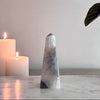 Decorative crystal obelisk on a marble surface with candles and a plant in the background.