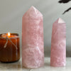 Two rose quartz crystal towers with a lit candle on a neutral background