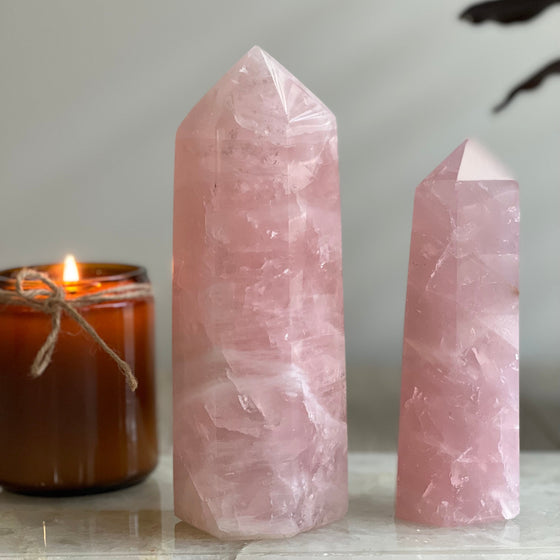 Two rose quartz crystal towers with a lit candle on a neutral background