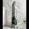 A green agate tower-like mineral formation on a marble surface.
