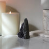 A side view of a natural amethyst freestanding crystal on  a white marble base featuring candles in the background.