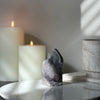 Two lit candles and a natural rainbow amethyst crystal on a white surface with a neutral background