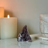 A natural rainbow amethyst crystal featured on a marble white platform with candles in the background.