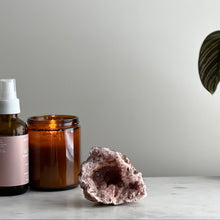  Amber glass jar, bottle with white cap, and pink crystal on a light surface with a neutral background