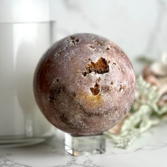 Pink Amethyst sphere with blurred background featuring candle and flowers.