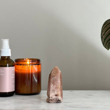  A bottle, a candle, and a crystal on a surface with a neutral background