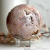 Round pinkish-brown Pink Amethyst Sphere on a clear stand with a blurred background.