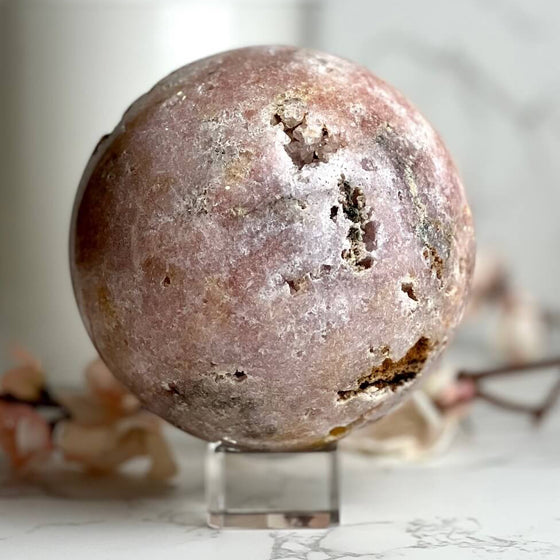 Round pinkish-brown Pink Amethyst Sphere on a clear stand with a blurred background.