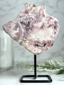  Pink Amethyst on stand with blurred background featuring a candle and flowers.