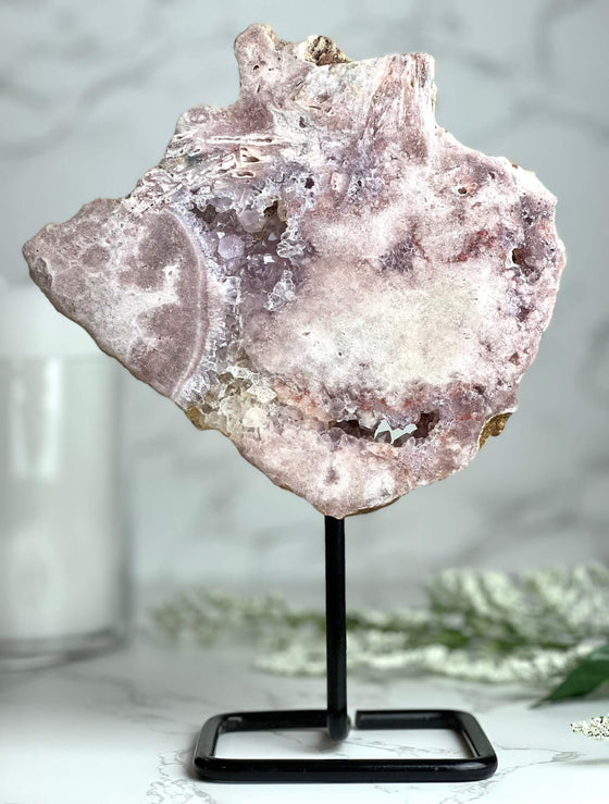 Pink Amethyst on stand with blurred background featuring a candle and flowers.
