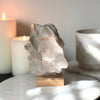 Pink Himalayan Samadhi Quartz on a wooden and silver stand with a blurred background featuring candles and a book.