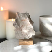  Pink Himalayan Samadhi Quartz on a wooden and silver stand with a blurred background featuring candles and a book.
