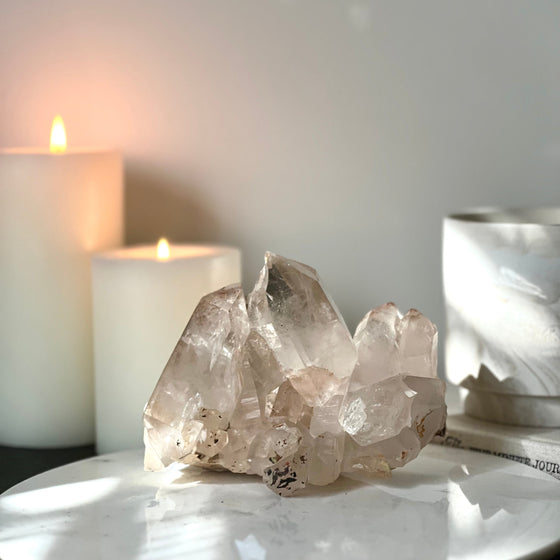 Pink Himalayan Samadhi Quartz on a white marble pedestal and a blurred background featuring candles and a book.
