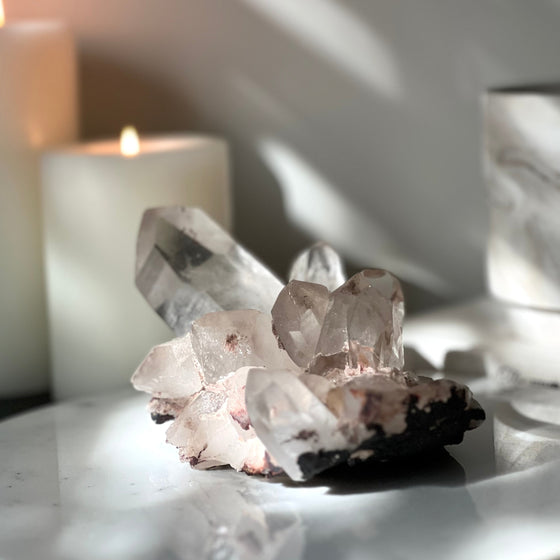 Pink Himalayan Quartz Cluster on white stand with blurred background featuring a book and candles.