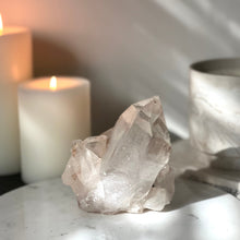  Pink Himalayan Samadhi Quartz on a marble stand with candles and a book in the background.
