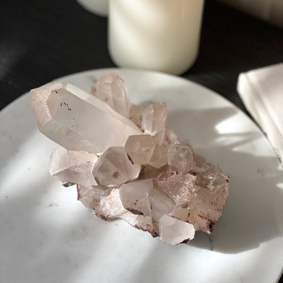 Pink Himalayan Quartz Cluster on white stand with blurred background featuring a book and candles.
