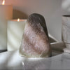Decorative Rainbow Amethyst crystal on a reflective surface with candles in the background