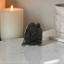  Decorative dark gray crystal on a marble surface with a lit candle in the background