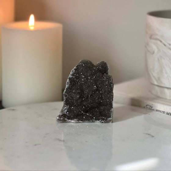 Decorative dark gray crystal on a marble surface with a lit candle in the background