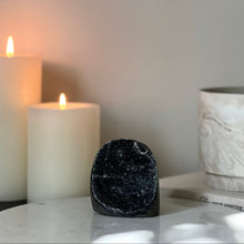  Gray black rainbow amethyst, white candle, and decorative pot on a surface with a neutral background