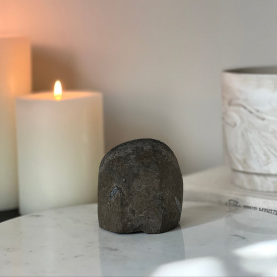 Decorative stone, lit candle, and ceramic vase on a marble surface with a neutral background