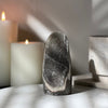 Decorative rainbow amethyst crystal on a surface with candles and a marble object in the background