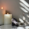 Natural Rainbow Amethyst crystal on white marble platform featuring candles in the background.