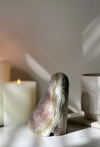 Decorative Rainbow Amethyst crystal on a reflective surface with candles in the background