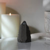 A rear view of a natural amethyst freestanding crystal on  a white marble base featuring candles in the background.