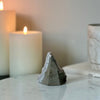 A rear view of a natural rainbow amethyst crystal featured on a marble white platform with candles in the background.