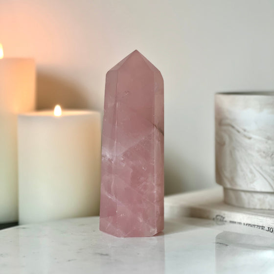Pink crystal tower on a marble surface with a candle and marble container in the background.