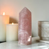Rose quartz crystal on a white surface with candles and a marble container in the background
