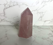  A small pink Rose Quartz crystal tower placed on a marble surface.
