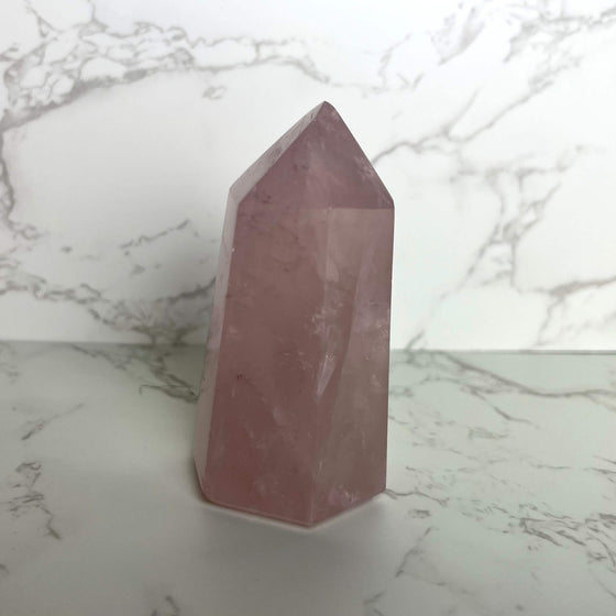 A small pink Rose Quartz crystal tower placed on a marble surface.