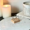 A small silver and wood crystal stand displayed on marble pedestal with candles and a book in the background.