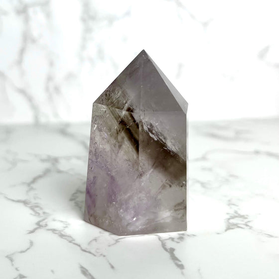 A smoky amethyst point crystal on a marble surface.