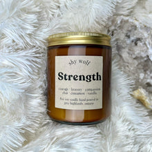  A brown jar of 'Strength' tarot candle by SKY WOLF, surrounded by white furry material and a crystal on a furry surface.